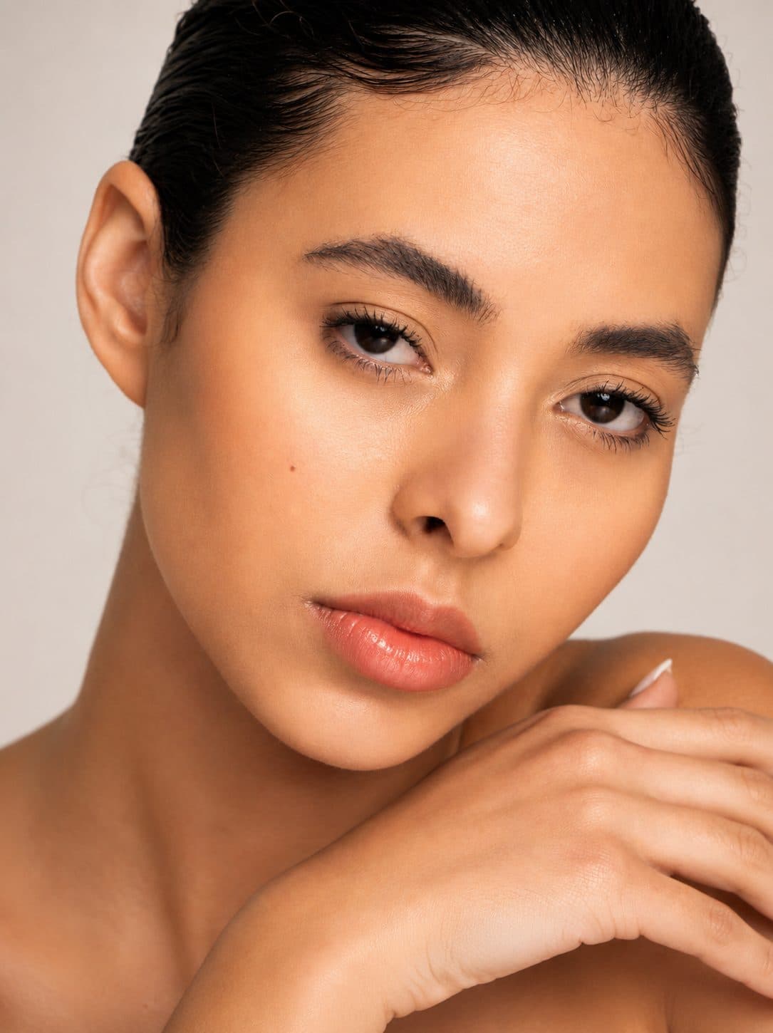 Clean beauty portrait, slicked-back hair, hand resting on shoulder, direct gaze