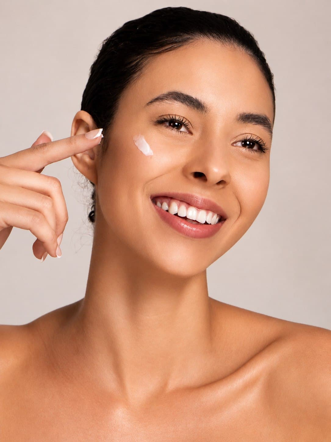 Beauty campaign portrait of Jess applying cream to her cheek, soft studio light