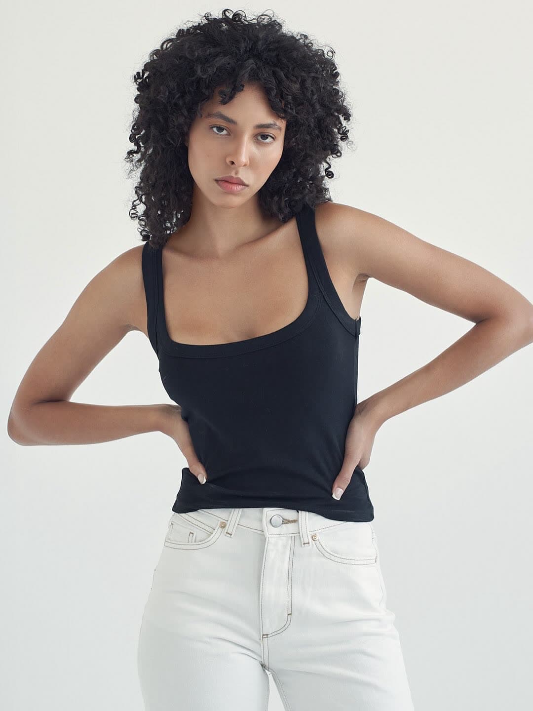 Test frame: Jess in a black tank and white jeans, hands on her hips