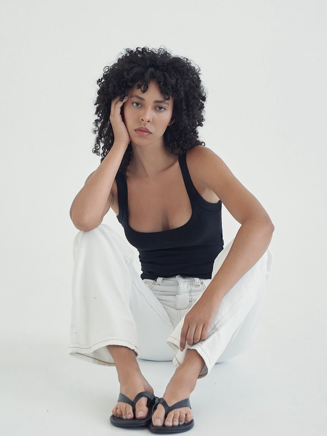 Test frame: Jess seated on the floor in white jeans, hand resting against her head