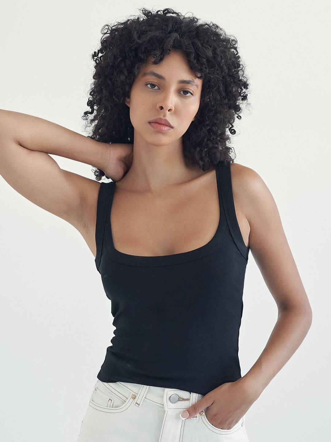 Test frame: Jess with a hand behind her neck, black tank and white jeans