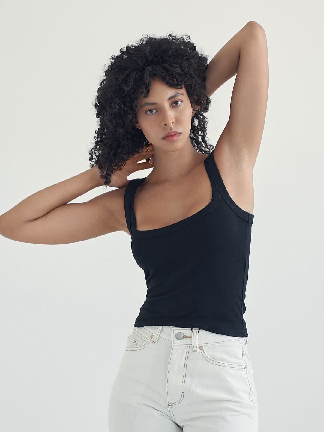 Test frame: Jess with one arm raised over her head, black tank and white jeans