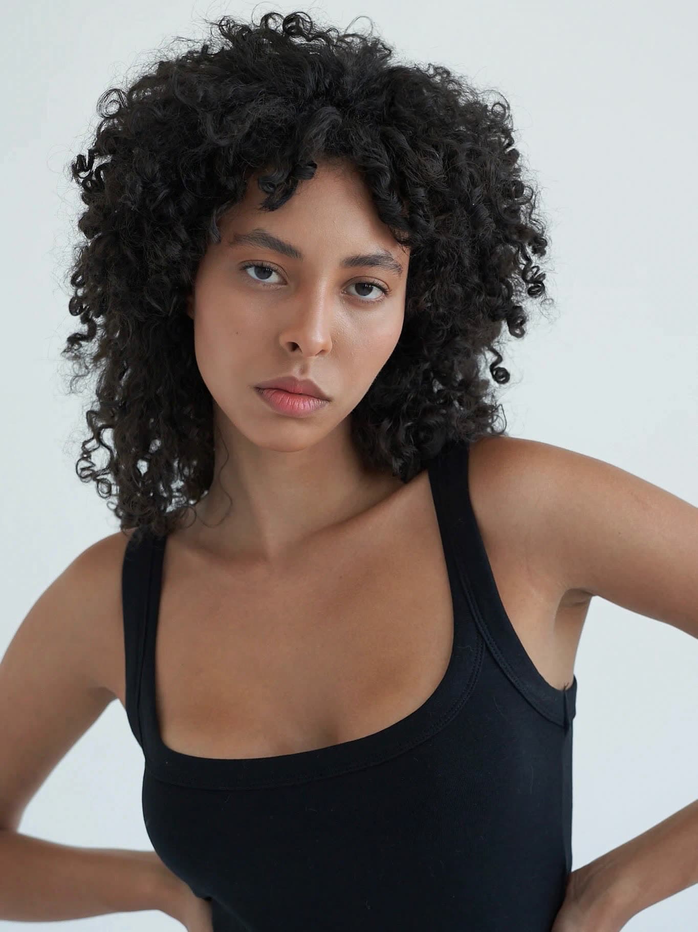 Test frame: waist-up in a black tank, hands on hips, full natural curls