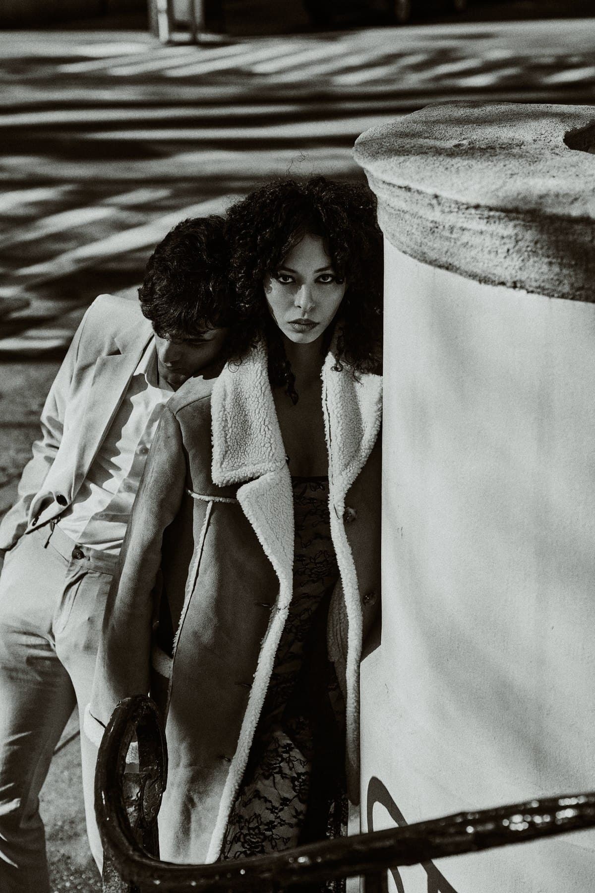 Jess crouched in a long black coat, monochrome portrait, curls loose