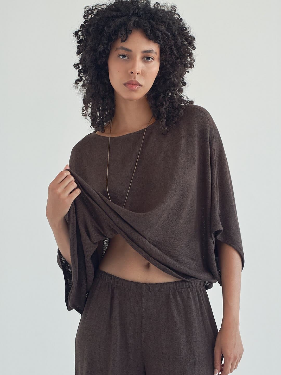 Test frame: Jess lifting the hem of the mocha knit top, wide-leg trousers