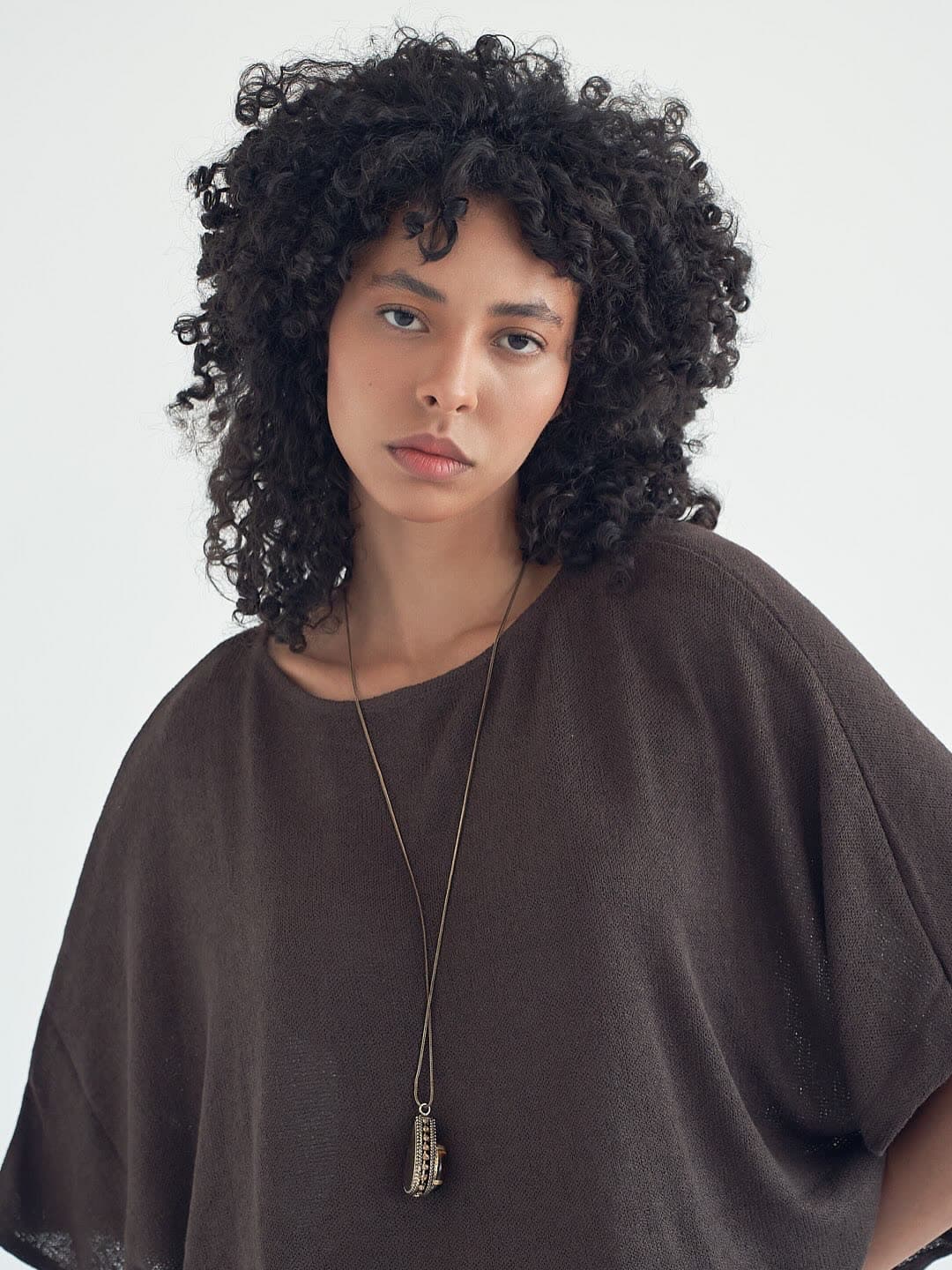 Test frame: Jess in an oversized mocha knit top with a long pendant, natural curls