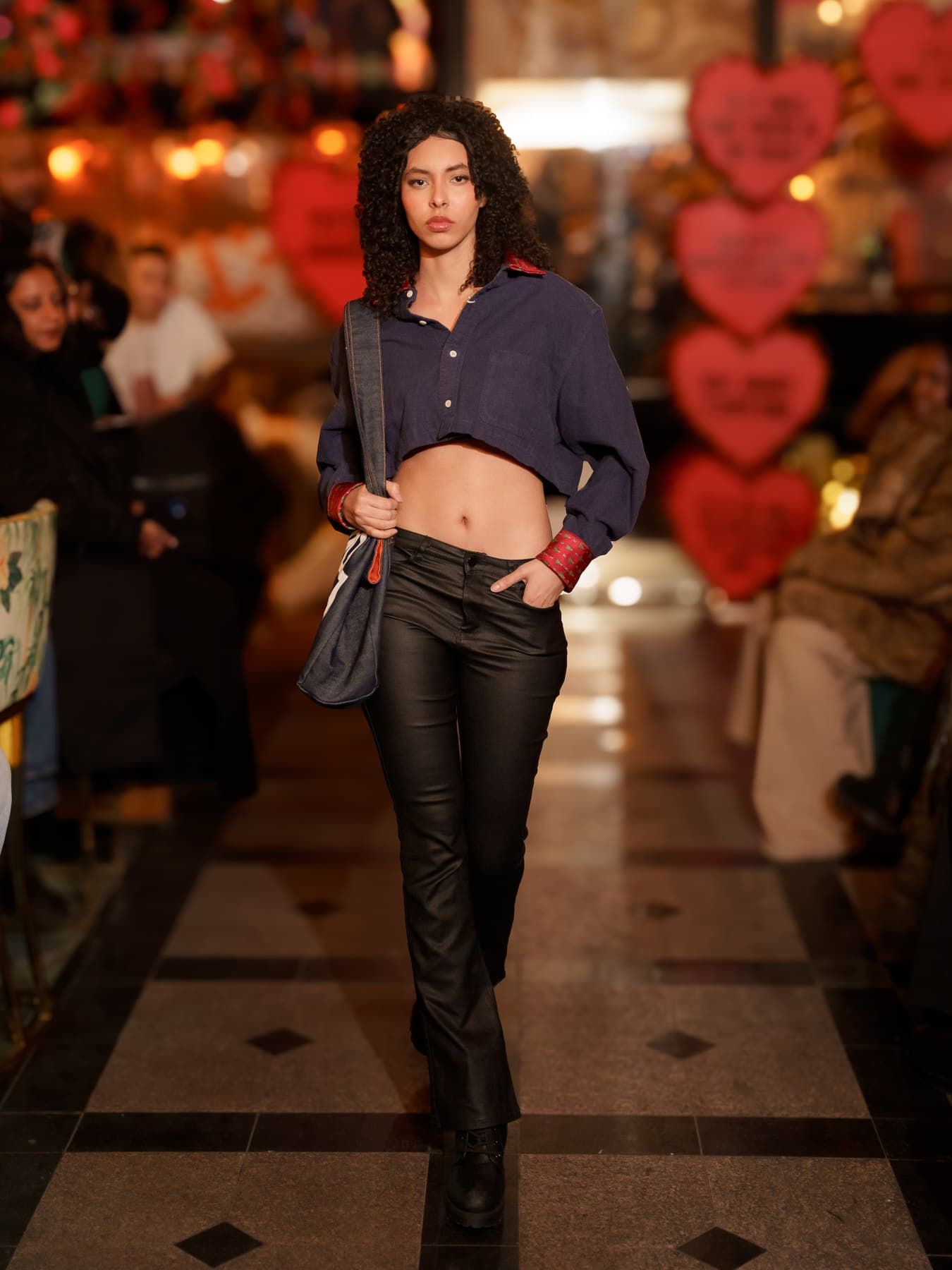 Jess walking through a night market strung with string lights, cropped jacket and boots
