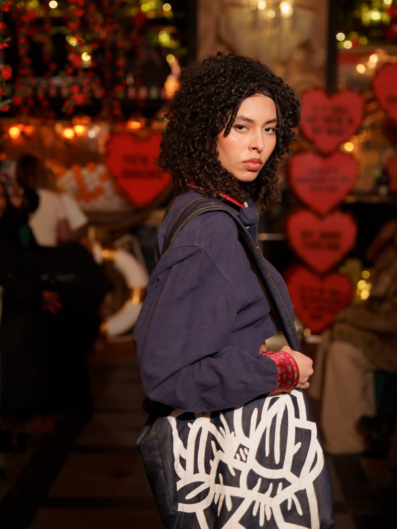 Jess in a slit dress walking through a heart-lantern-lit market corridor