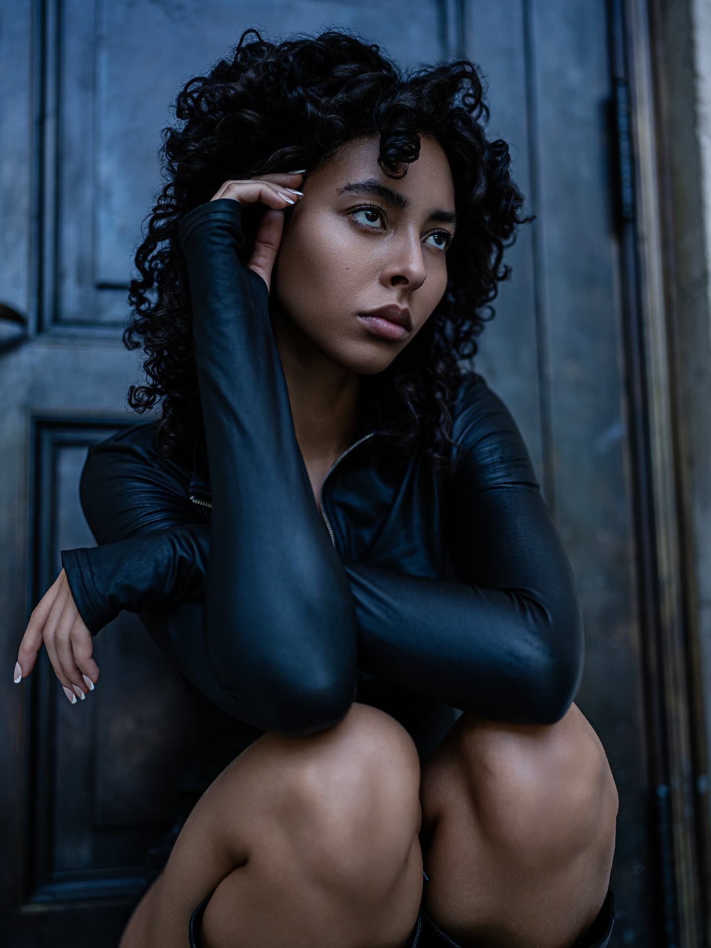 Jess crouched with arms folded over her knees in the black leather jacket, moody blue light