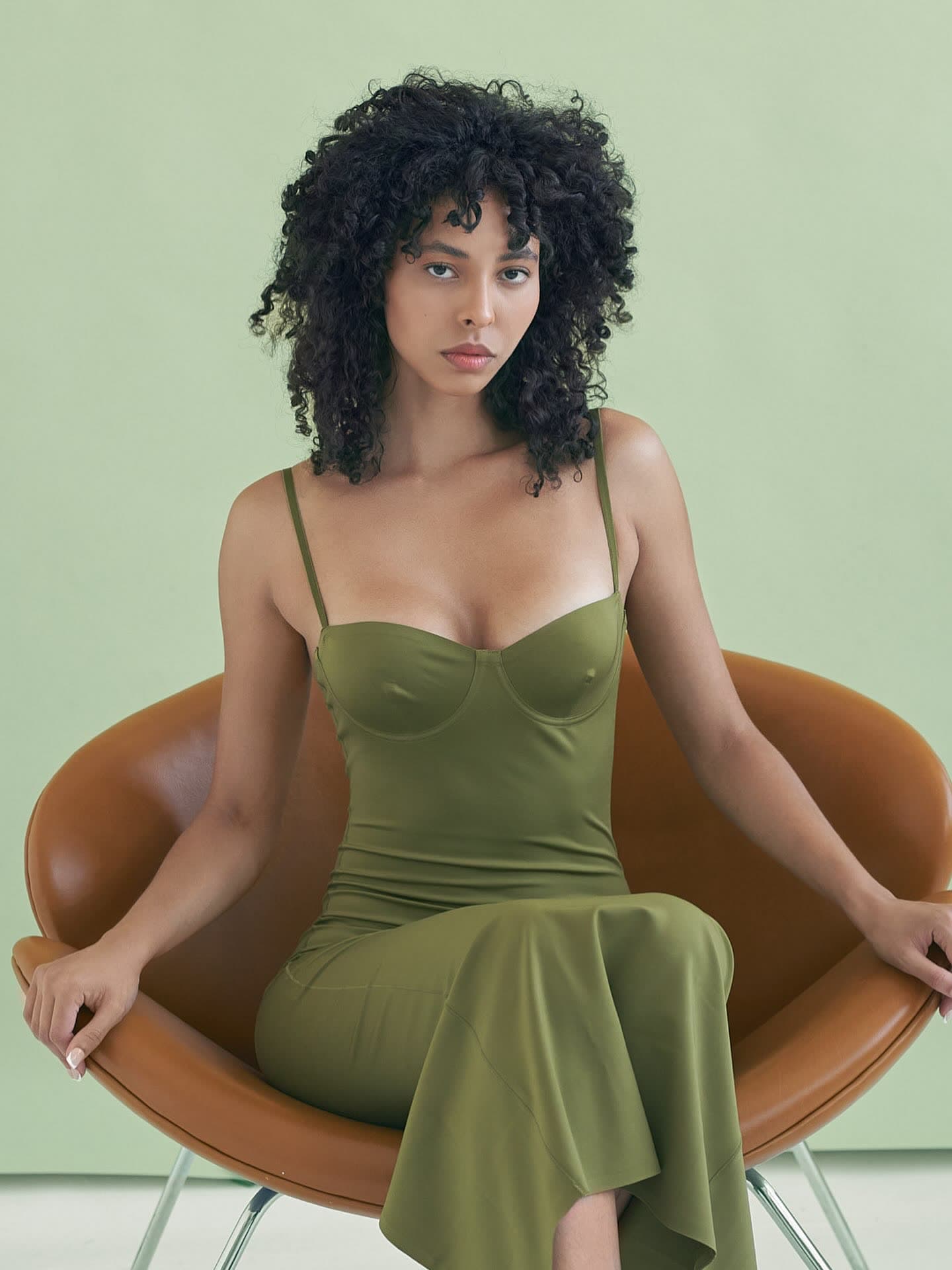 Jess seated in a tan leather chair in the olive dress, skirt draped to the floor
