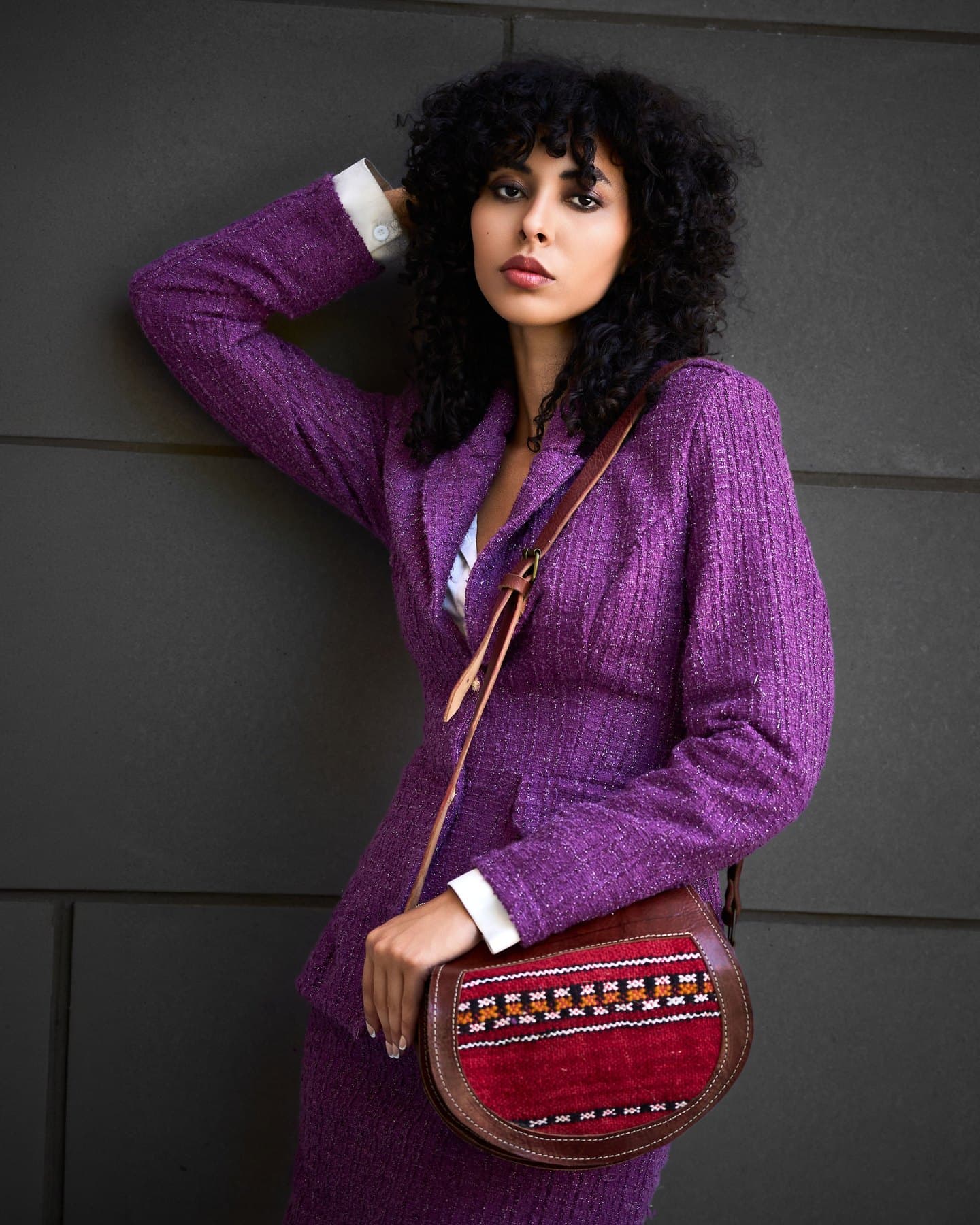 Full-length portrait of Jess in a violet tweed suit, hand raised to her curls