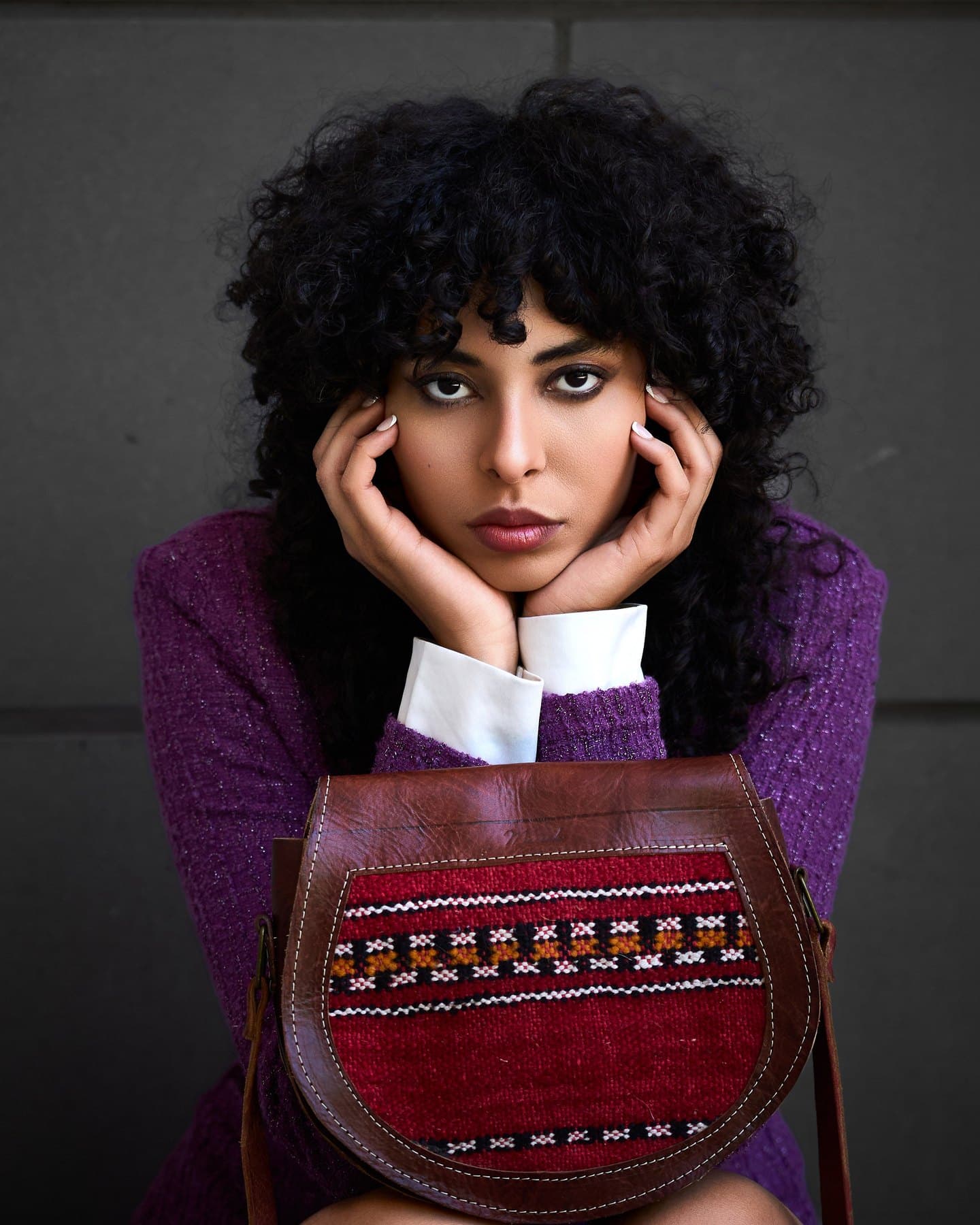 Close crop of Jess crouched, chin resting on hands over the woven bag